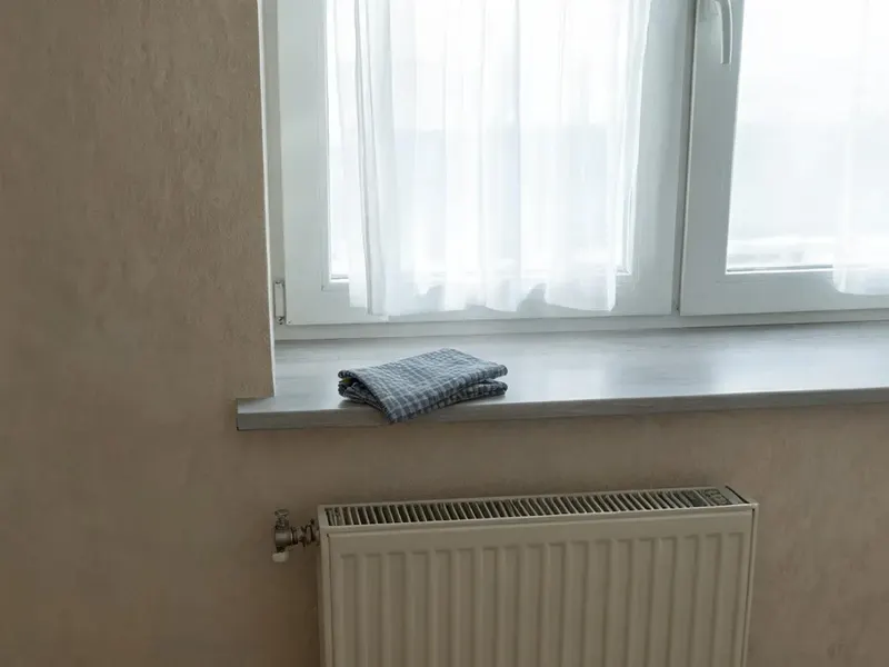 Złożona ściereczka leży na czystym parapecie nad grzejnikiem, za oknem widać firankę