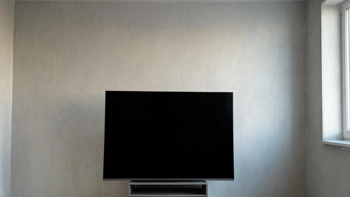 Duży telewizor z wyłączonym ekranem stoi samotnie na szafce pod pustą ścianą